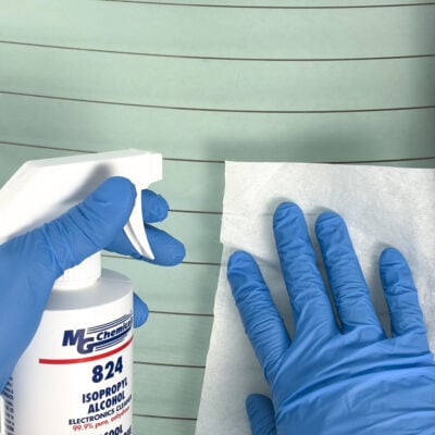 Lors d'une réparation de dégivrage de lunette arrière, une personne portant des gants en nitrile bleus nettoie la surface intérieure de ce dispositif avec de l'alcool isopropylique MG Chemicals 824. Ce nettoyant élimine la saleté et la graisse sans laisser de résidus, garantissant ainsi une bonne adhérence de la colle époxy conductrice.