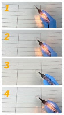 Lors d'une réparation du dégivreur arrière, une personne portant des gants bleus utilise une lampe témoin de 12 volts pour vérifier chaque ligne horizontale de la grille du dégivrage. La lampe allumée indique que la ligne est alimentée.