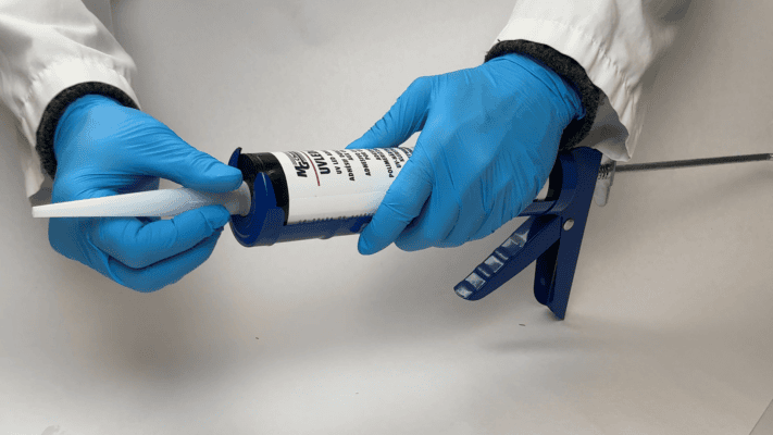 Gloved hands attaching an applicator tip to a caulking gun loaded with MG Chemicals UV adhesive.