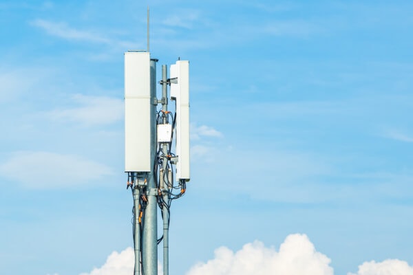 Cellular communication antenna mounted on a tower, with panel antennas and cabling visible against a clear blue sky.