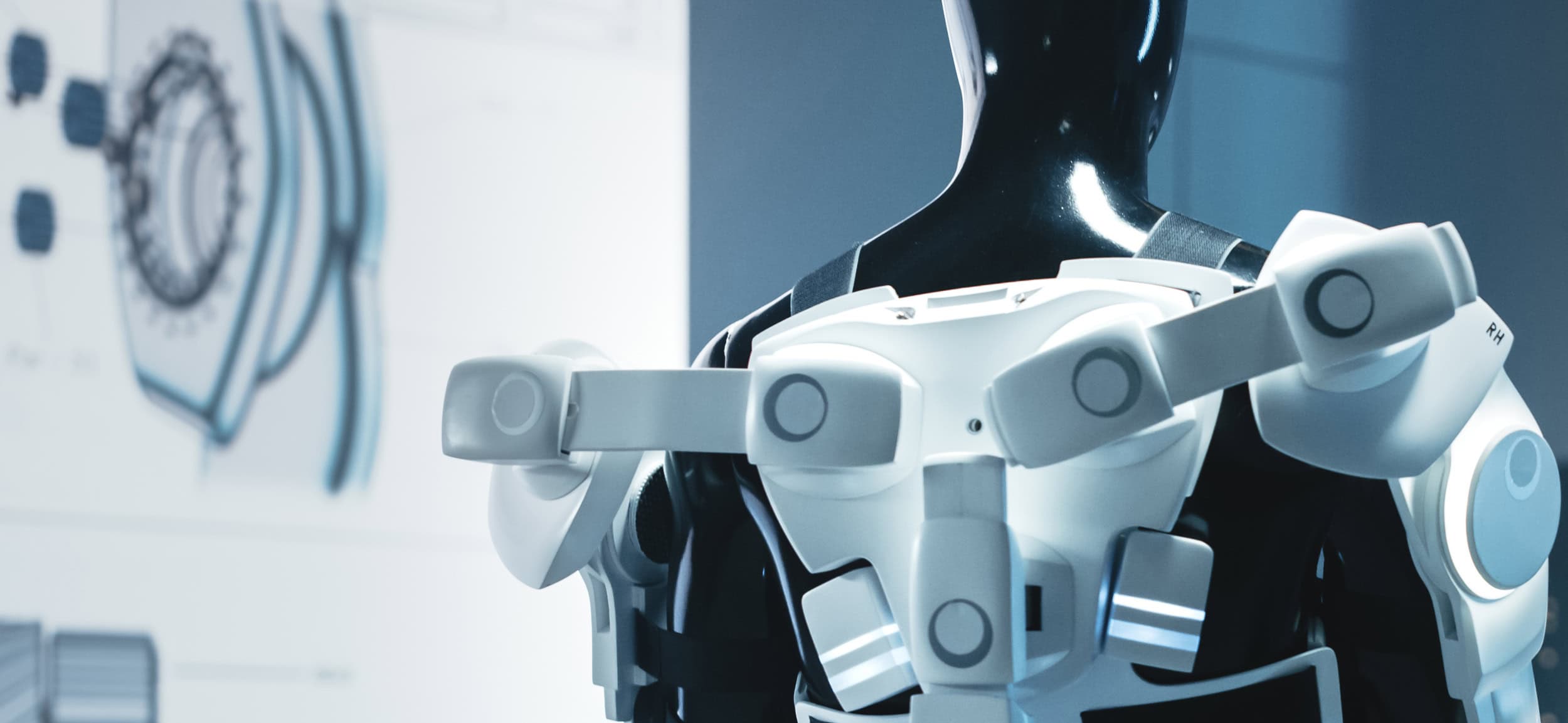 Futuristic military exoskeleton worn by a human figure, showing articulated shoulder, torso, and arm components in a laboratory or development setting.