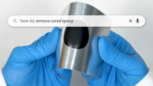 Gloved hands holding a curved piece of metal with a black patch of cured epoxy; a search bar overlay reads &lsquo;how to remove cured epoxy.&rsquo;